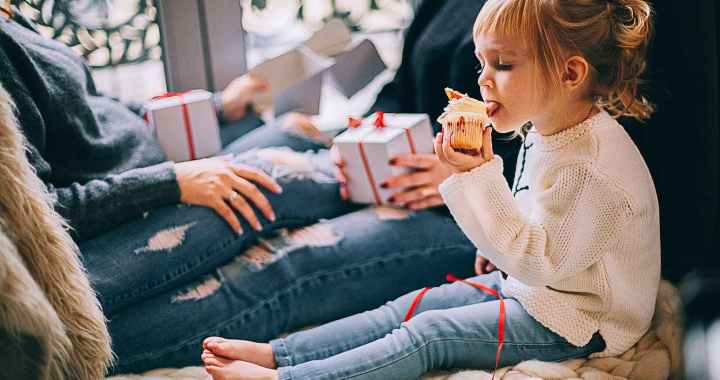 girl eating cupcake while sitting beside woman in blue denim distressed jeans